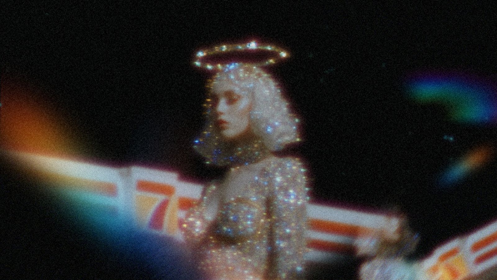 Surreal, grainy image of a sparkling figure with a glowing halo against a dark, cinematic background.