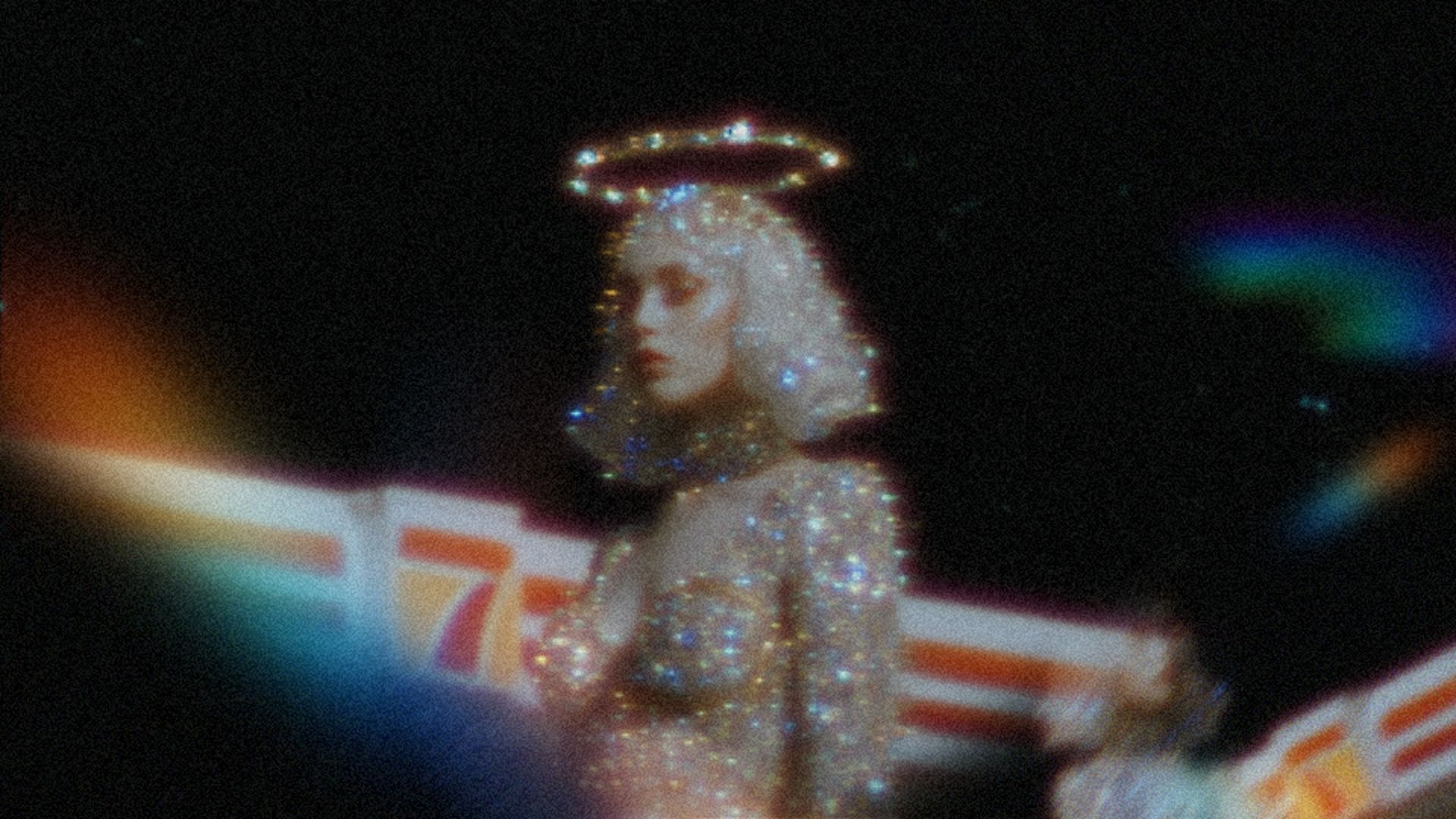 Surreal, grainy image of a sparkling figure with a glowing halo against a dark, cinematic background.