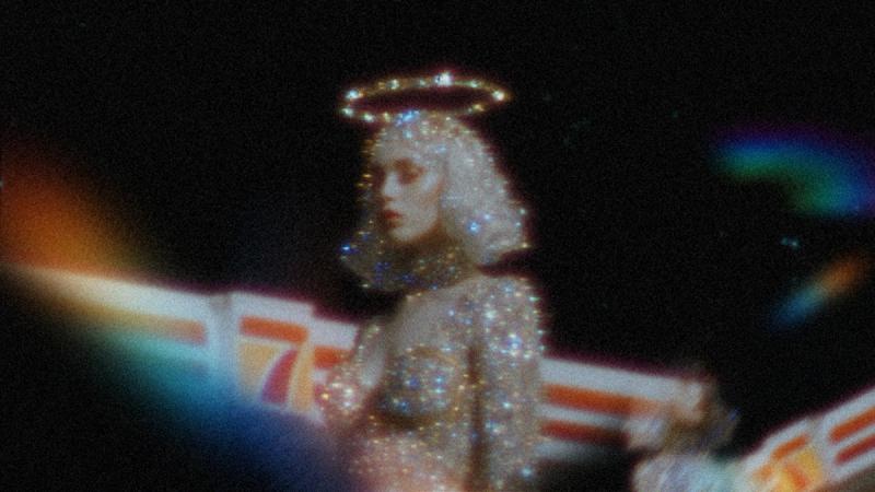 Surreal, grainy image of a sparkling figure with a glowing halo against a dark, cinematic background.