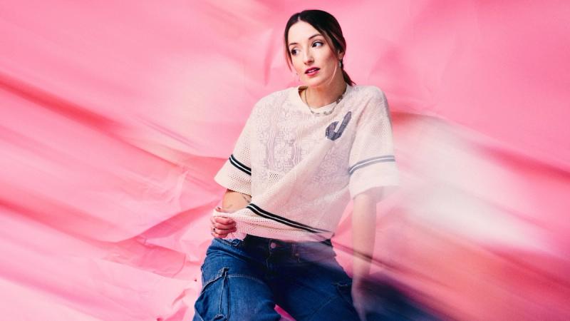 sad alex seated against a pink backdrop with translucent pink fabric moving across the foreground.