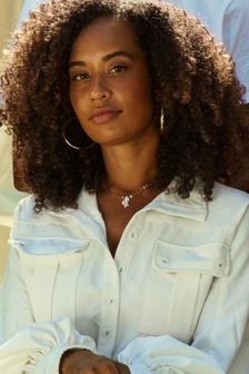 Young black woman with curly hair and in a white jumper sits and faces camera