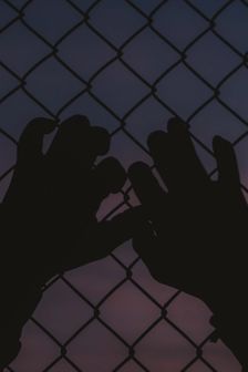 Against purple sky, hands reach up against fence