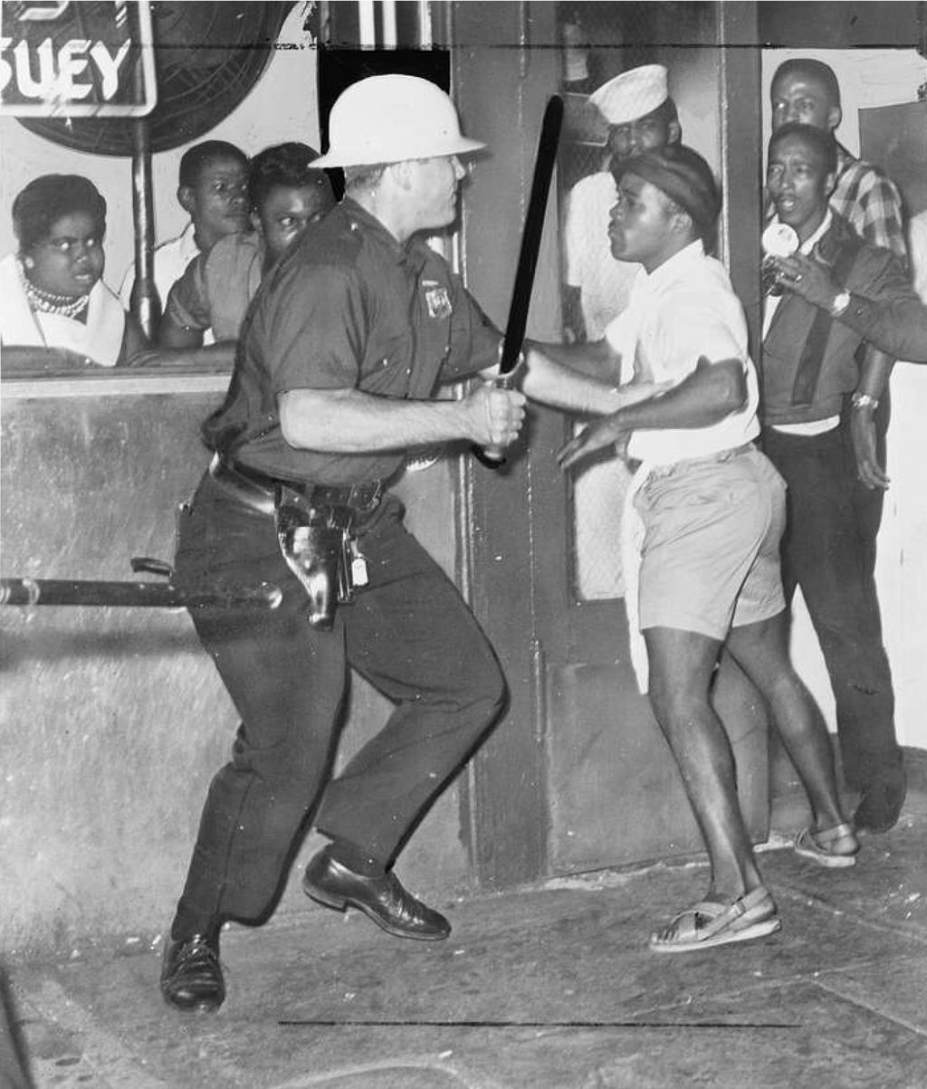 Police officer lifts a police baton at a young black man
