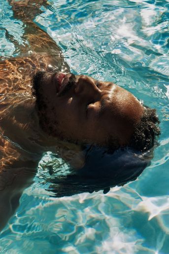 Young black man floating in pool of water peacefully swimming