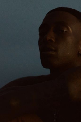 Close crop of black man's face while he looks defiantly into camera, sitting down at the beach 