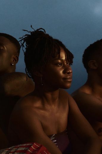 Young black woman sits between two friends at beach, staring into sunset