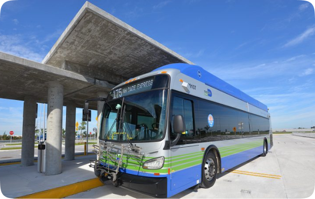 A blue and silver articulated bus parked at a bus stop under a concrete shelter. The bus has the words "175 DADE EXPRESS" written on the front.