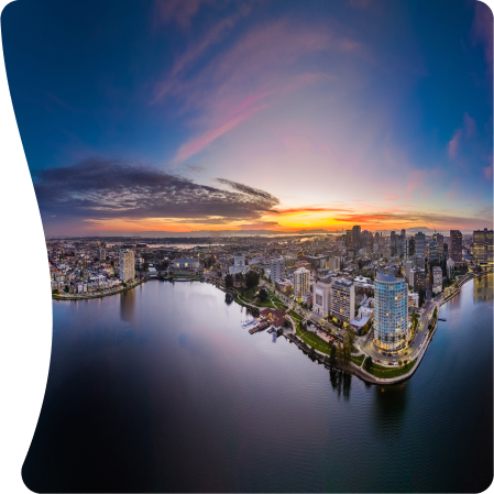 A panoramic view of the Oakland skyline at sunset, with lake shimmering in the foreground and a vibrant sky reflecting the city lights.