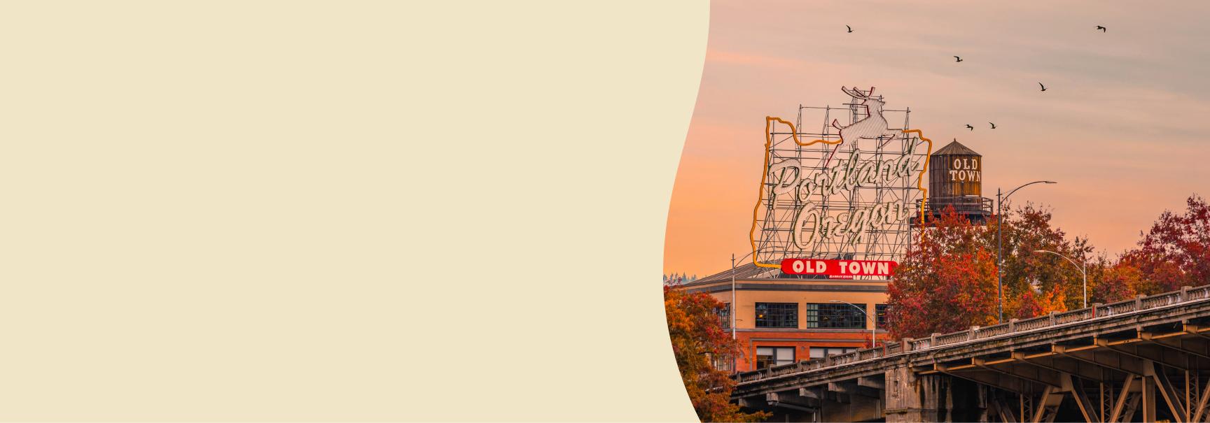 The iconic "Portland Oregon" sign glows against a warm sunset sky in the Old Town district. Colorful autumn trees and a few birds in flight add to the picturesque urban scene.