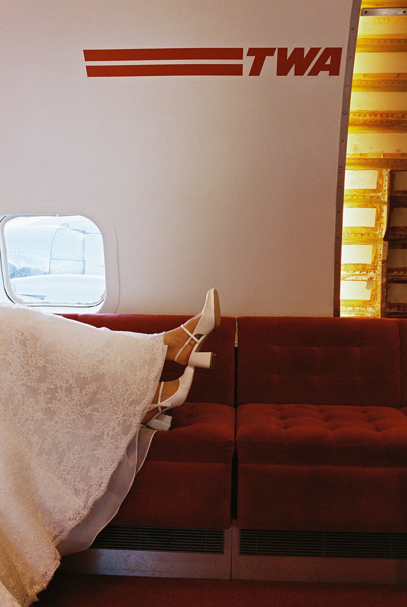 Bride's heels resting on the red velvet seats of the TWA airplane beneath the TWA logo