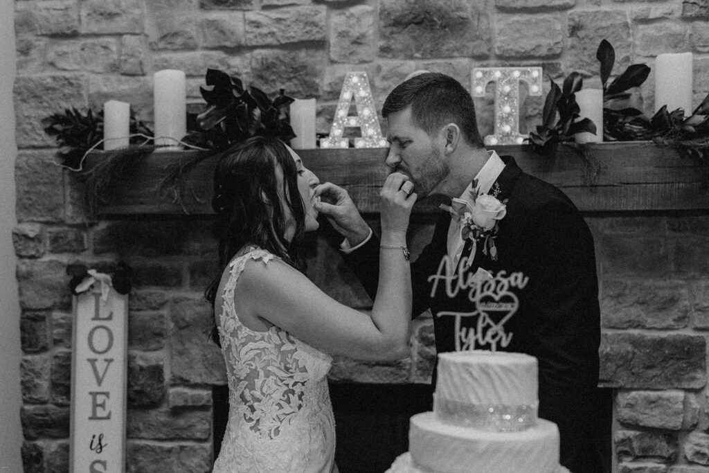Bride and groom feeding each other cake during their wedding reception at Chimney Oaks Golf Club, with a custom light-up sign in the background