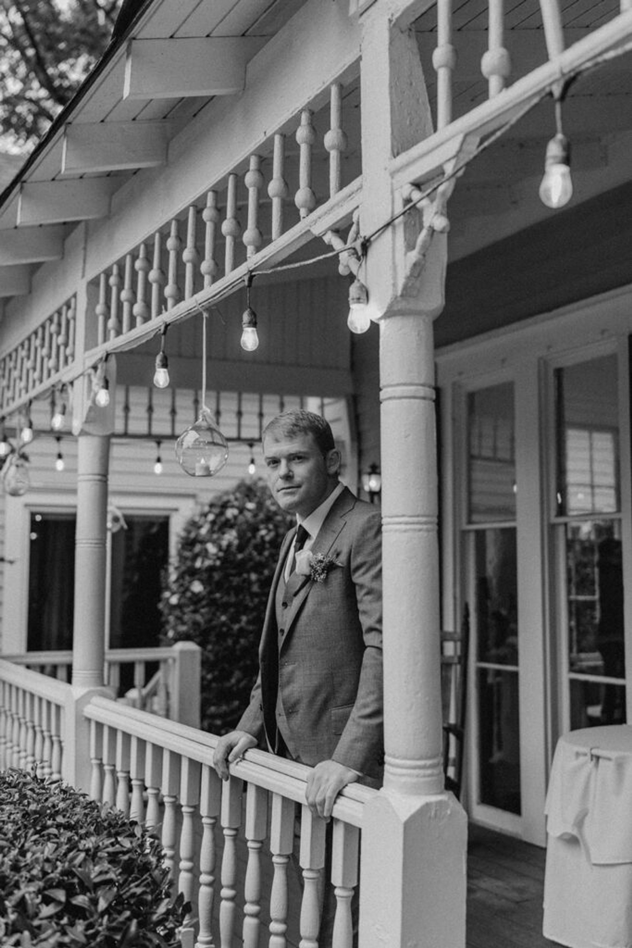 Scott stands on the porch of 173 Carlyle House, gazing thoughtfully ahead, with string lights hanging above