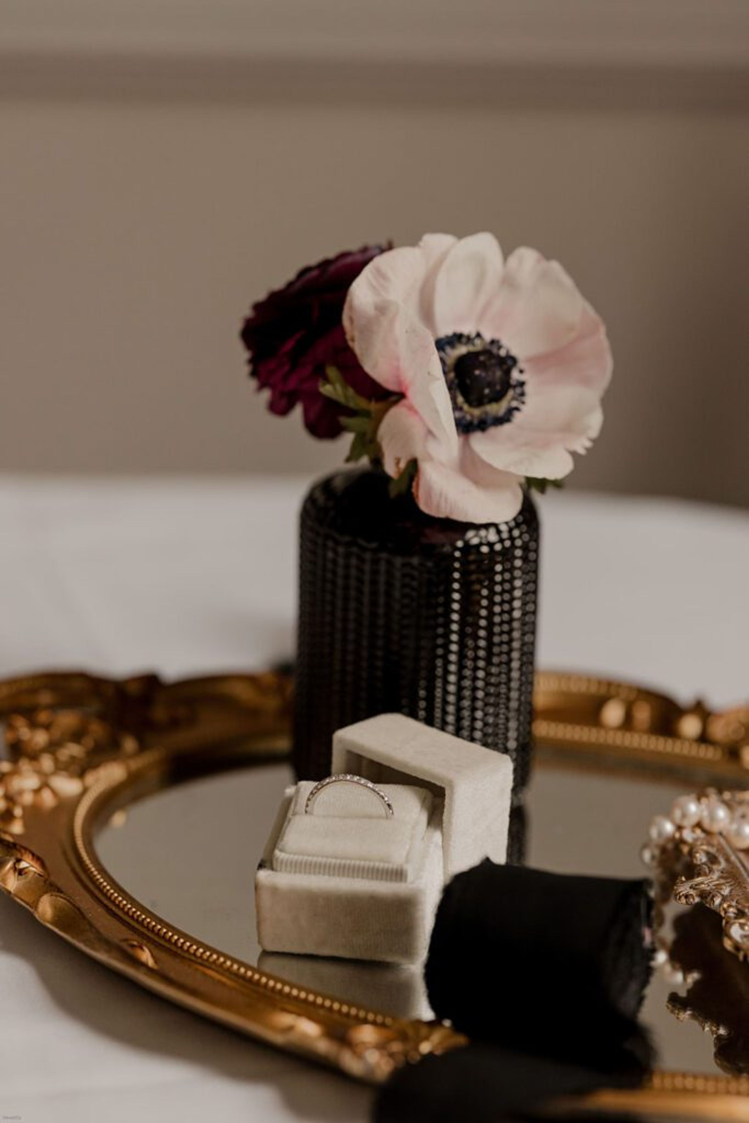A delicate flower arrangement in a black vase sits on a gold tray next to a ring box, capturing the elegant details of the wedding at 173 Carlyle House.
