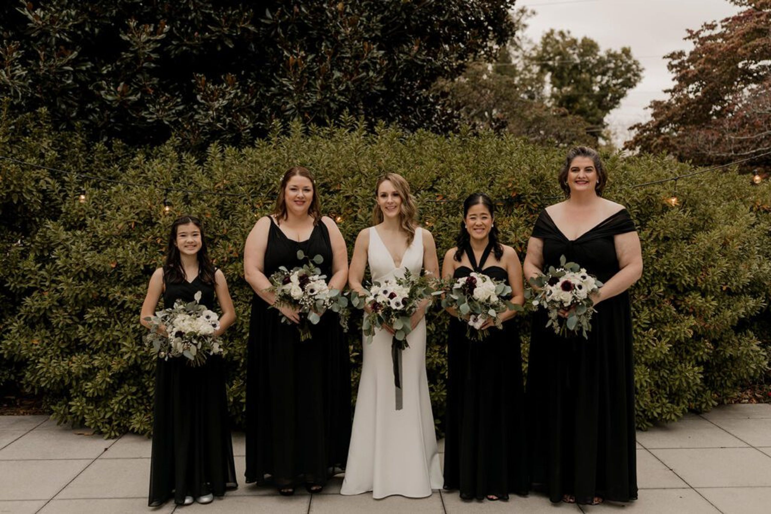 Deb stands with her bridesmaids, all holding bouquets, in the garden at 173 Carlyle House