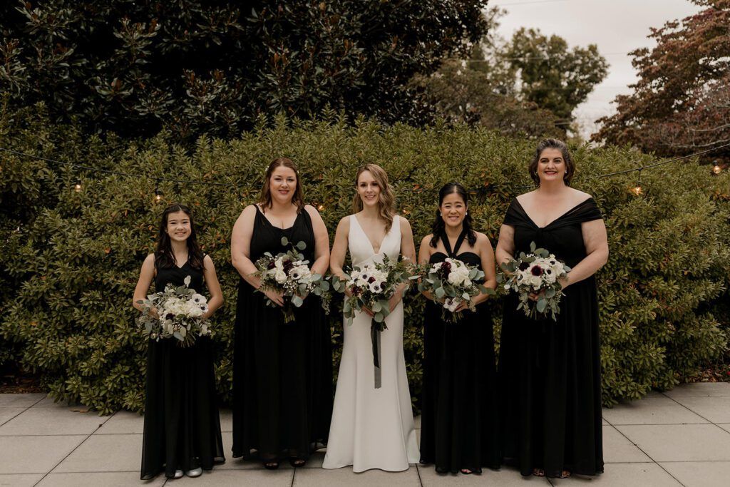 Deb stands with her bridesmaids, all holding bouquets, in the garden at 173 Carlyle House
