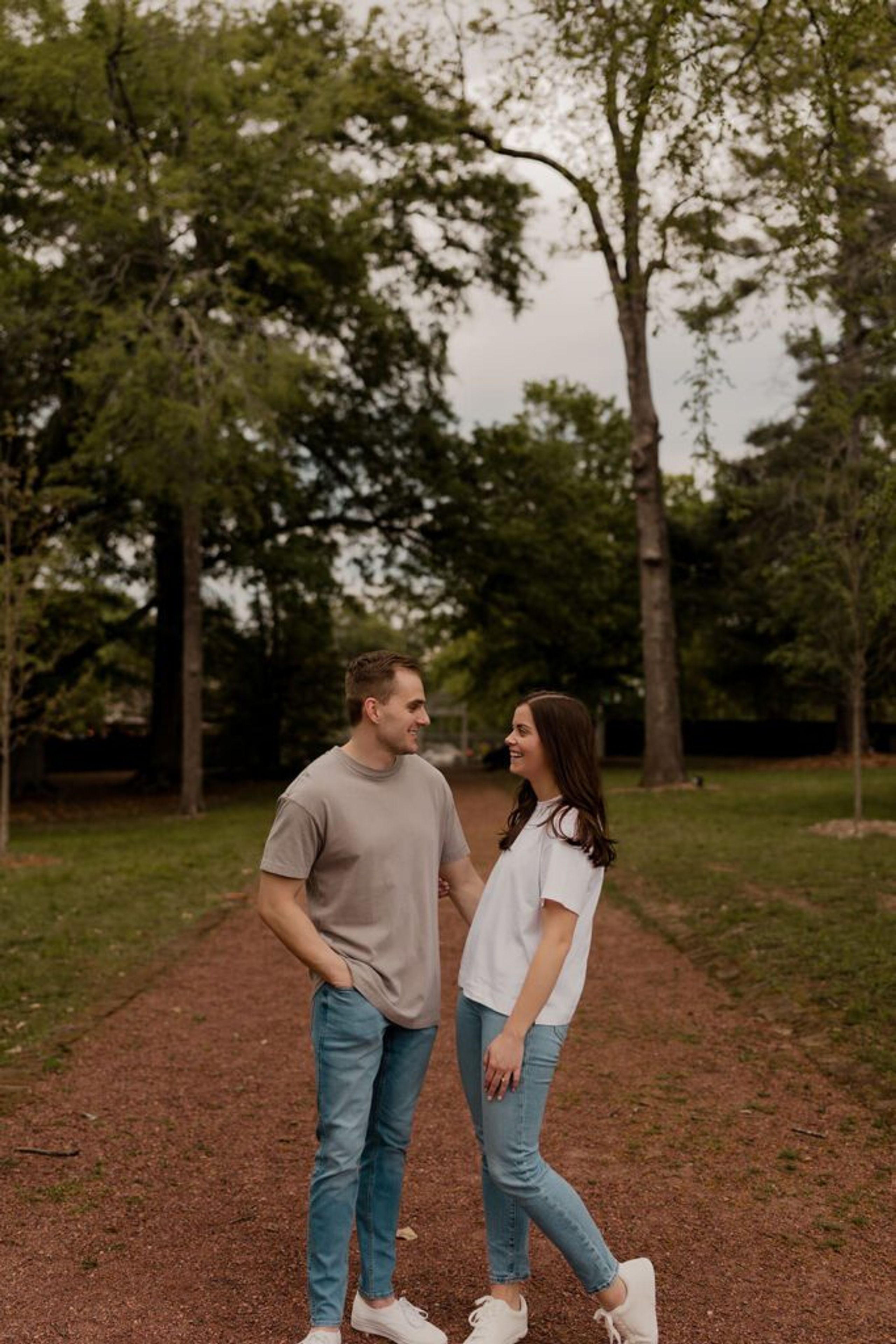 Casual couple walking and smiling in a park during their engagement photoshoot in relaxed outfits.