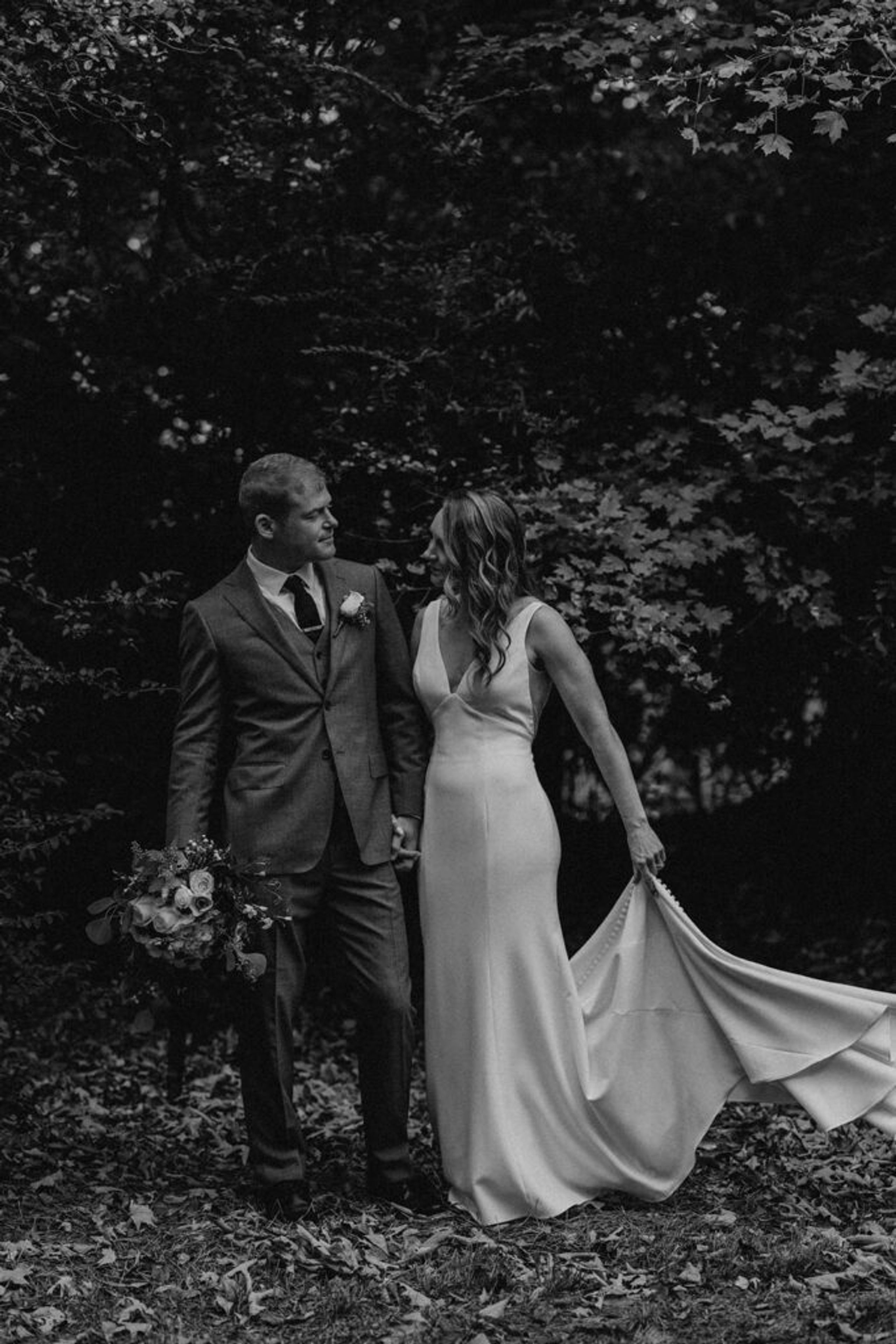 Scott and Deb stroll through a wooded area at 173 Carlyle House, Deb gracefully holding up her dress.