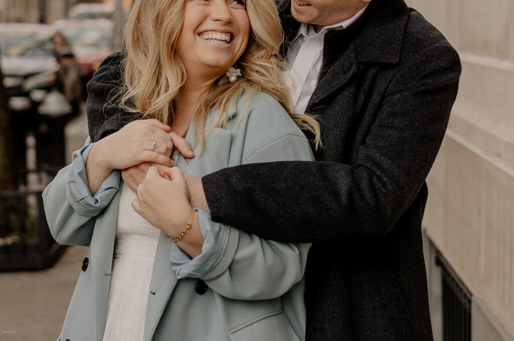 Couple smiling and embracing during their engagement photoshoot in stylish winter outfits.