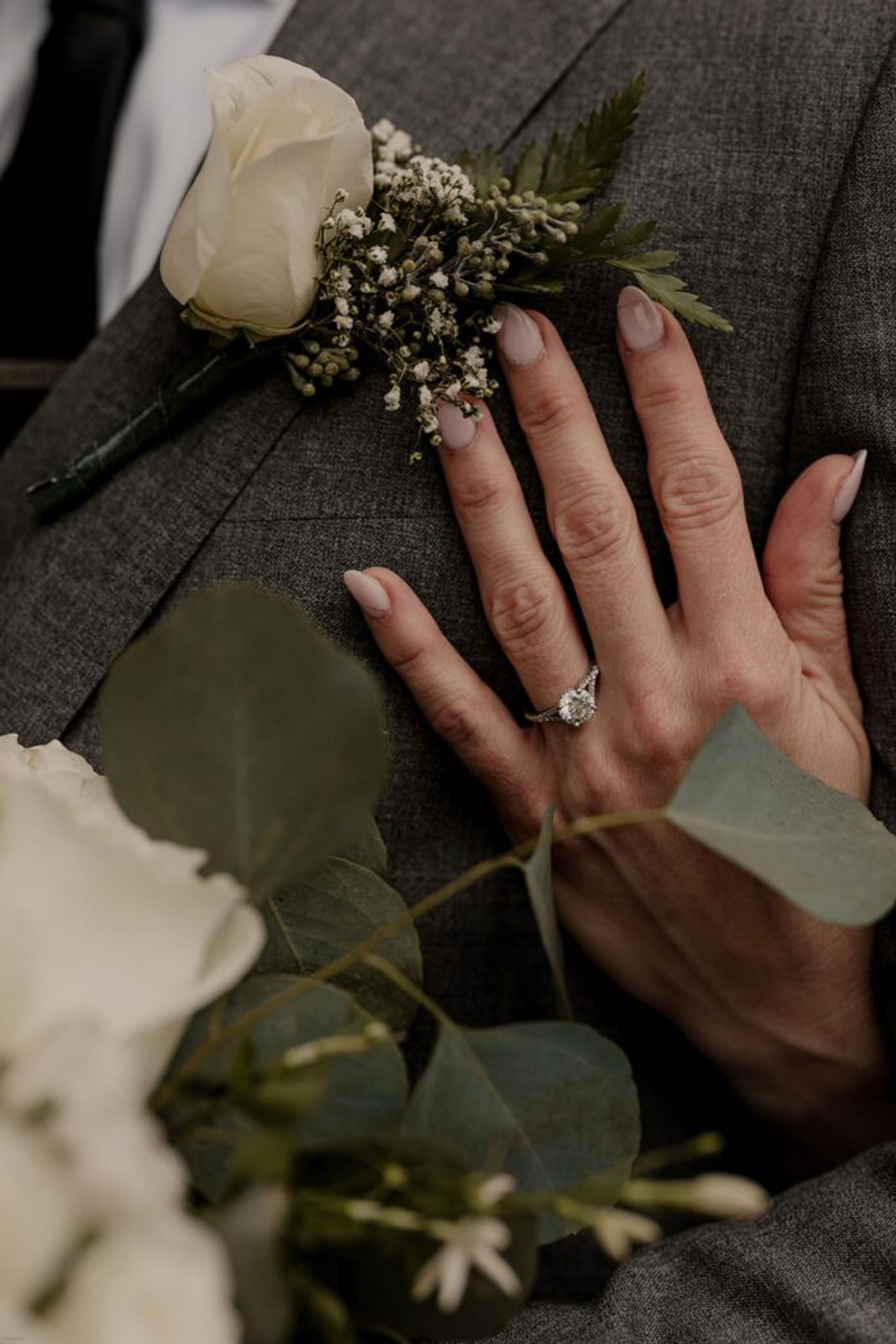 A close-up shot of Deb’s hand resting on Scott’s chest at 173 Carlyle House, showcasing her engagement ring and wedding bouquet.