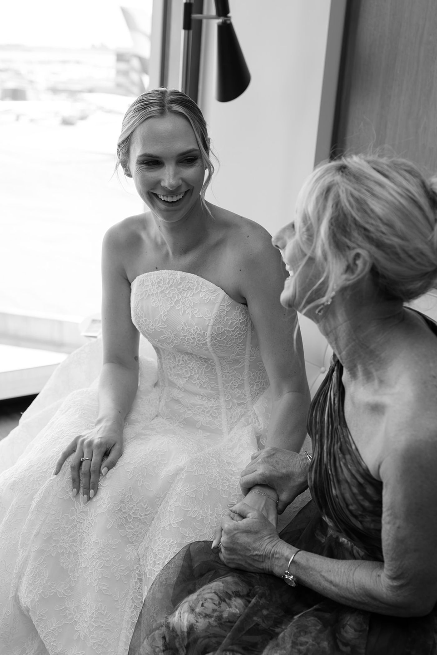 Black and white photograph of a bride laughing with her mother while getting ready at the TWA Hotel, JFK