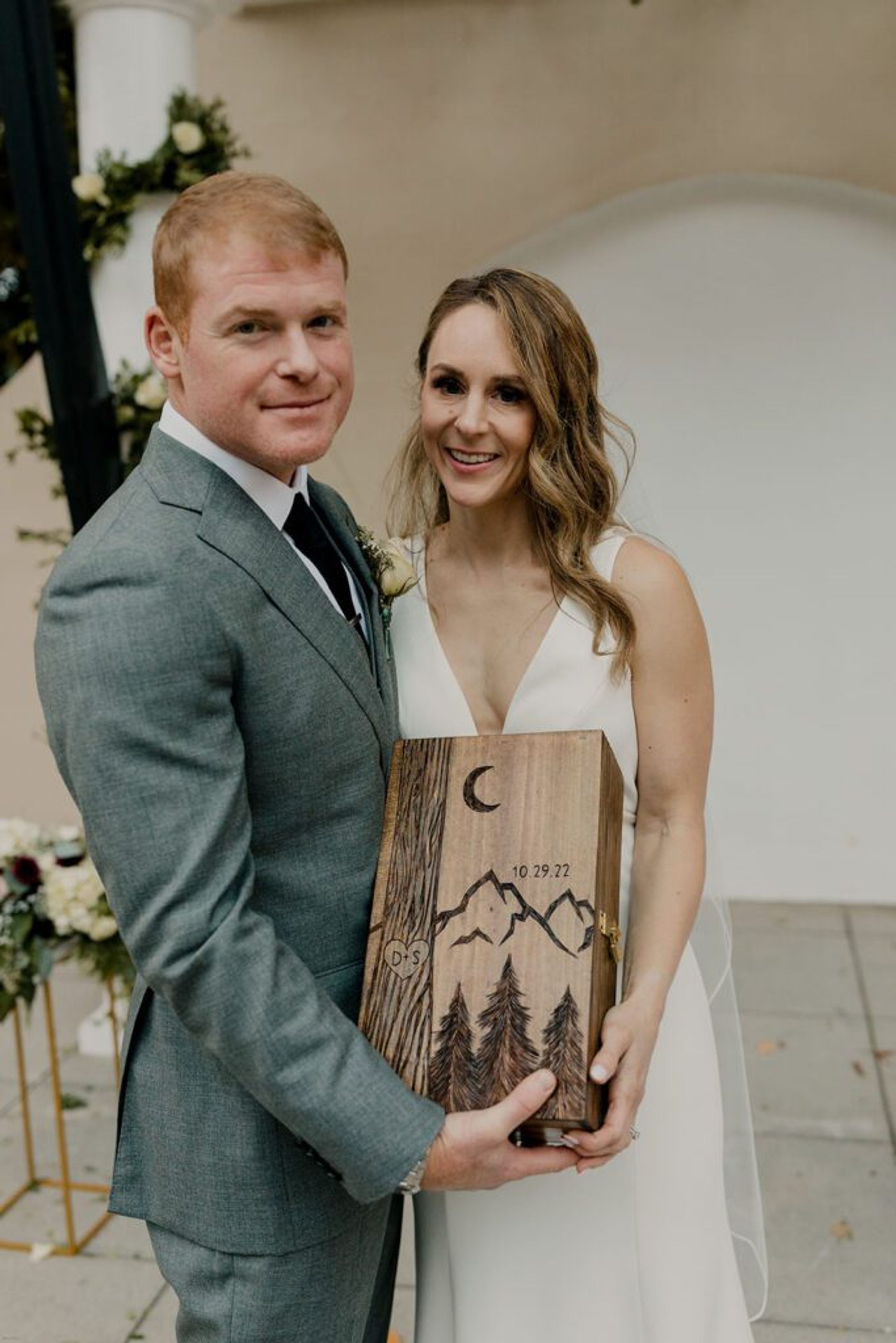 Scott and Deb hold an engraved wooden piece commemorating their wedding day at 173 Carlyle House
