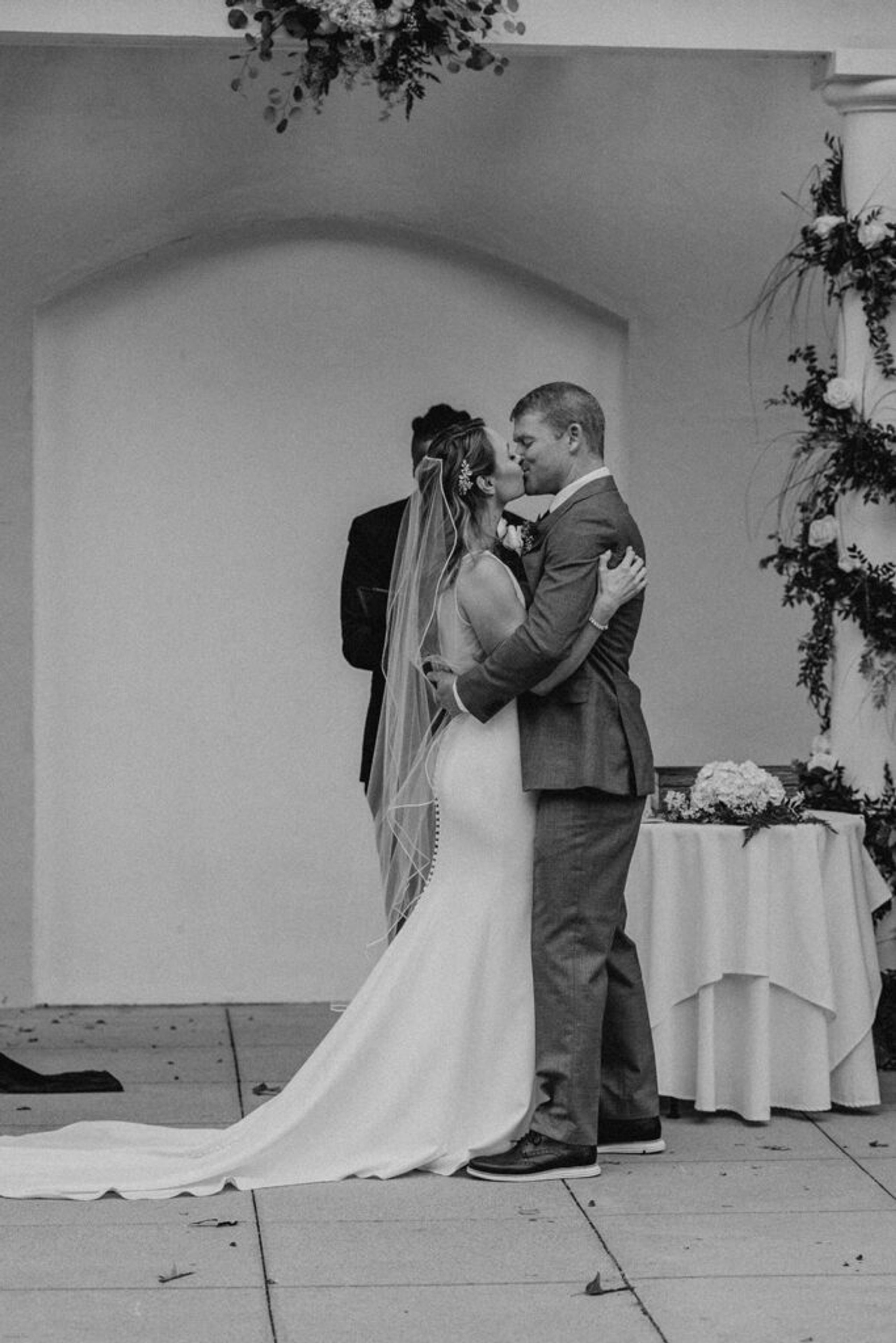 Scott and Deb kiss in front of the altar at 173 Carlyle House, surrounded by floral arrangements