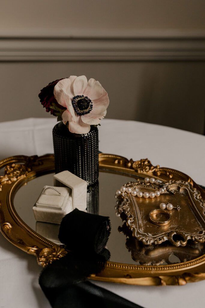A floral arrangement and ring box are elegantly displayed on a gold tray at 173 Carlyle House, showcasing wedding details.