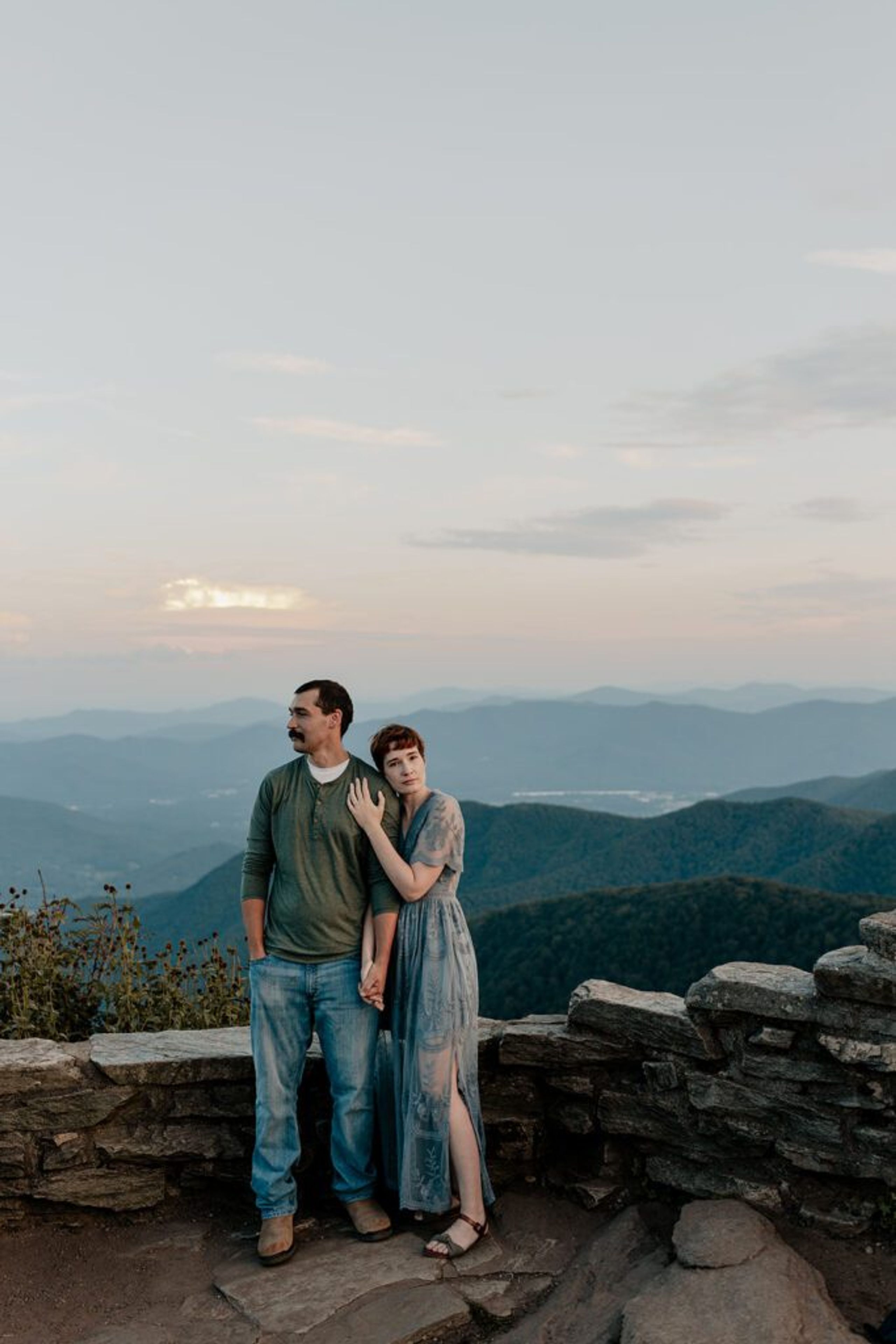 Couple standing at Craggy Pinnacle summit with mountain views during sunset engagement photos.