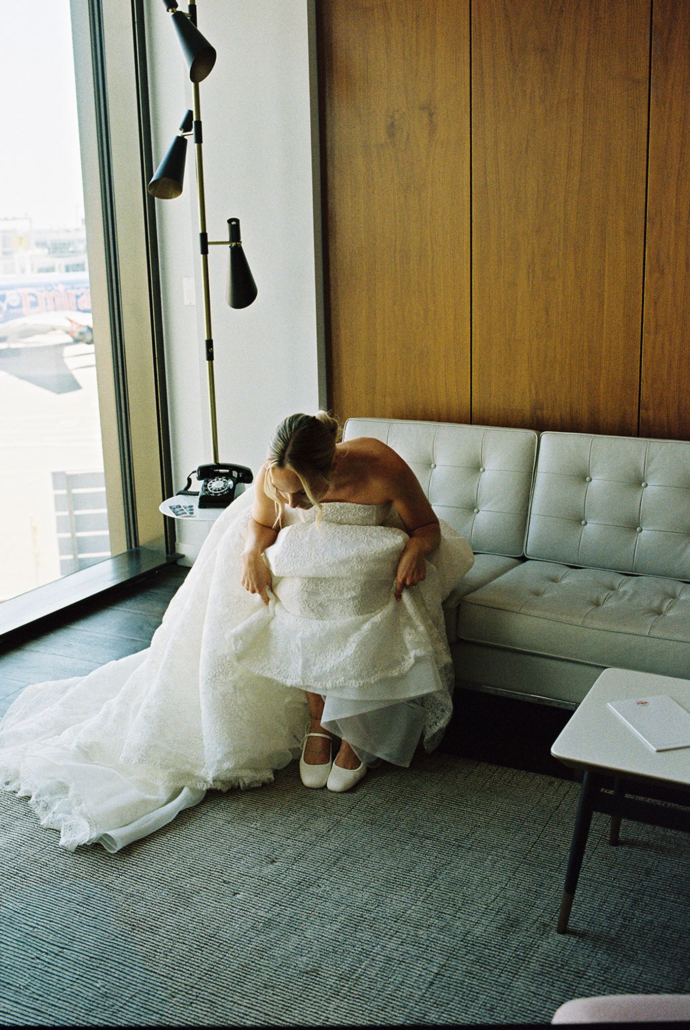 Bride stepping into her lace wedding gown by the window of a TWA Hotel guest room in New York