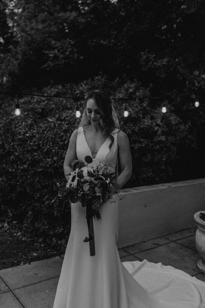Deb stands alone with her bouquet, smiling softly as she enjoys a quiet moment at 173 Carlyle House.