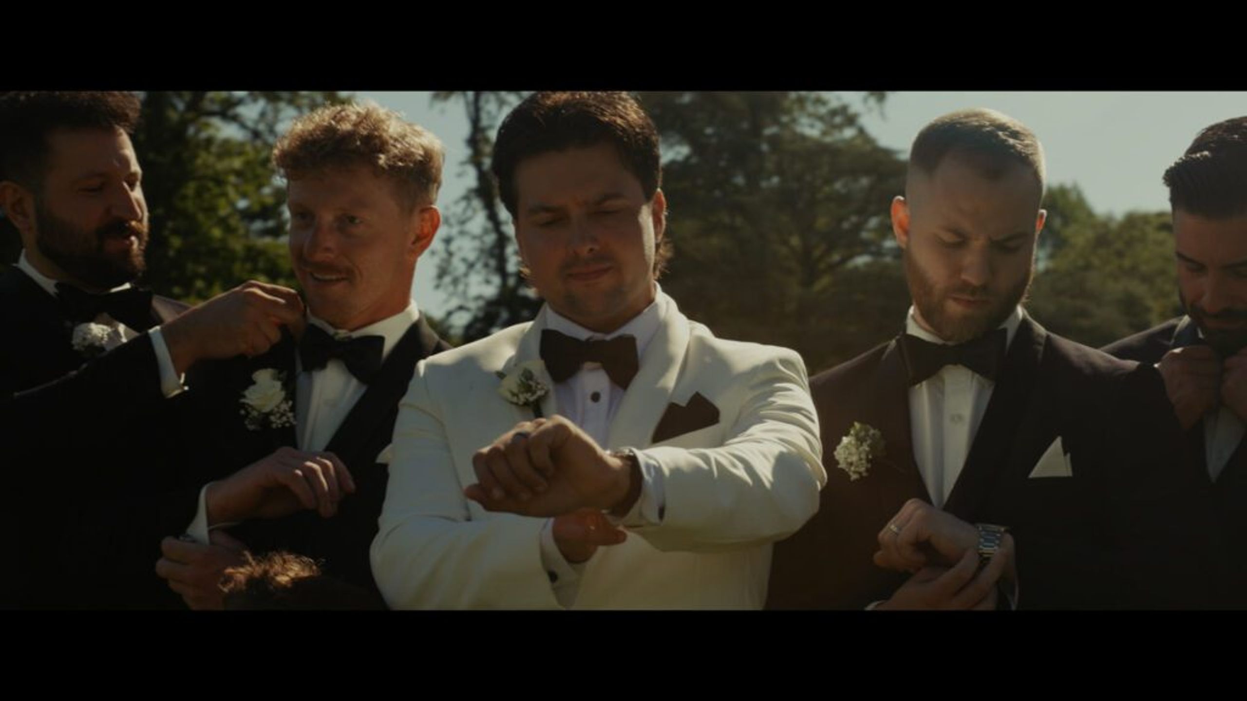 Groom with groomsmen in black tuxedos adjusting watches and bow ties before wedding at Old Westbury Gardens