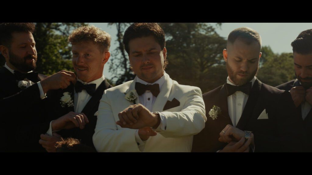 Groom with groomsmen in black tuxedos adjusting watches and bow ties before wedding at Old Westbury Gardens