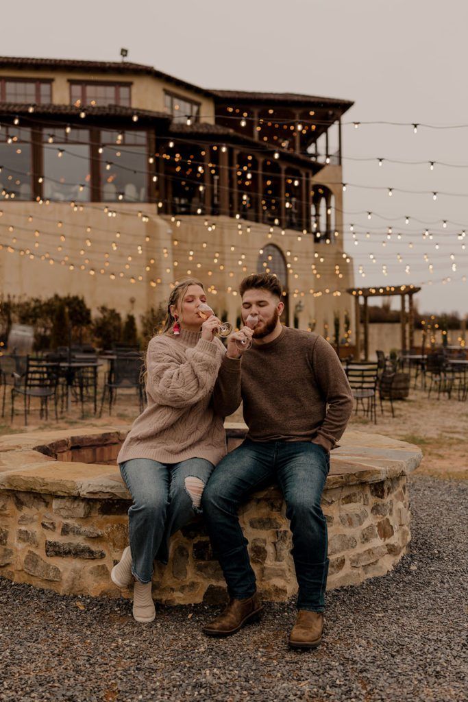 Taylor and Guillermo walking hand in hand by Tuscan-style architecture at Monteluce Winery, holding glasses of wine