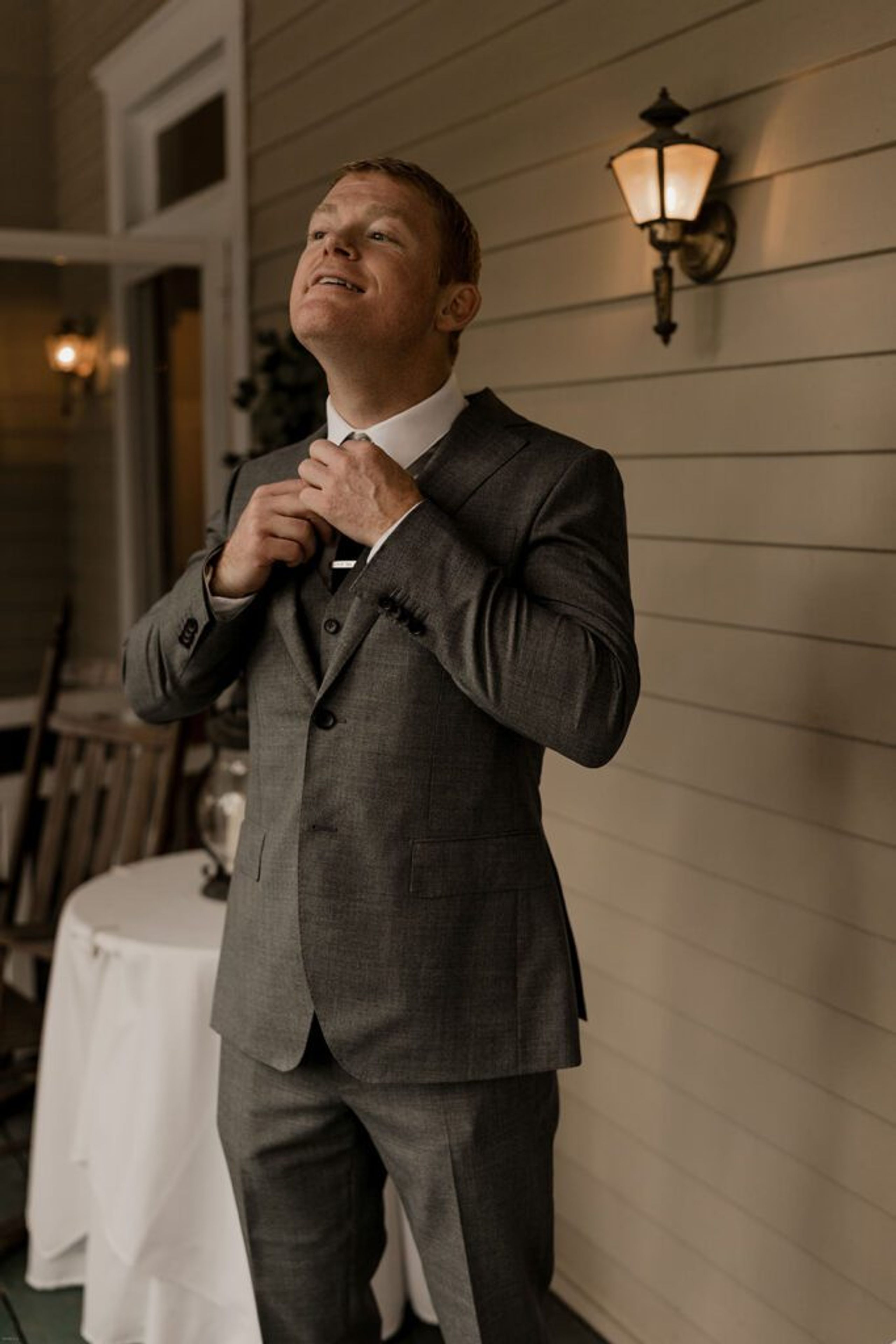 Scott adjusts his tie under the warm glow of a porch light at 173 Carlyle House, preparing for the ceremony.