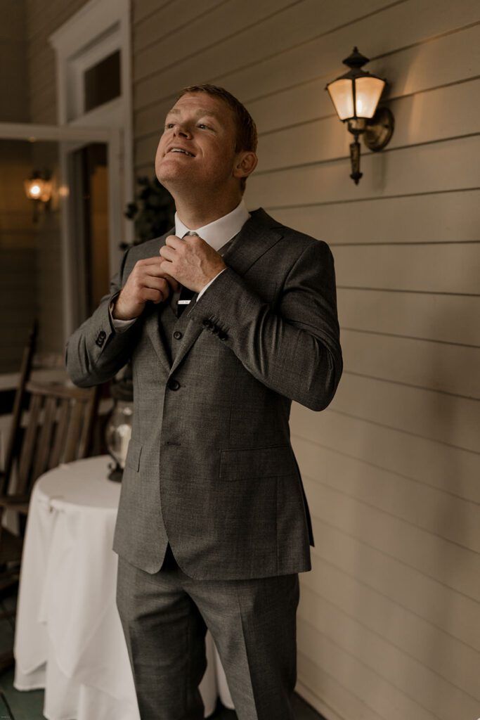 Scott adjusts his tie under the warm glow of a porch light at 173 Carlyle House, preparing for the ceremony.