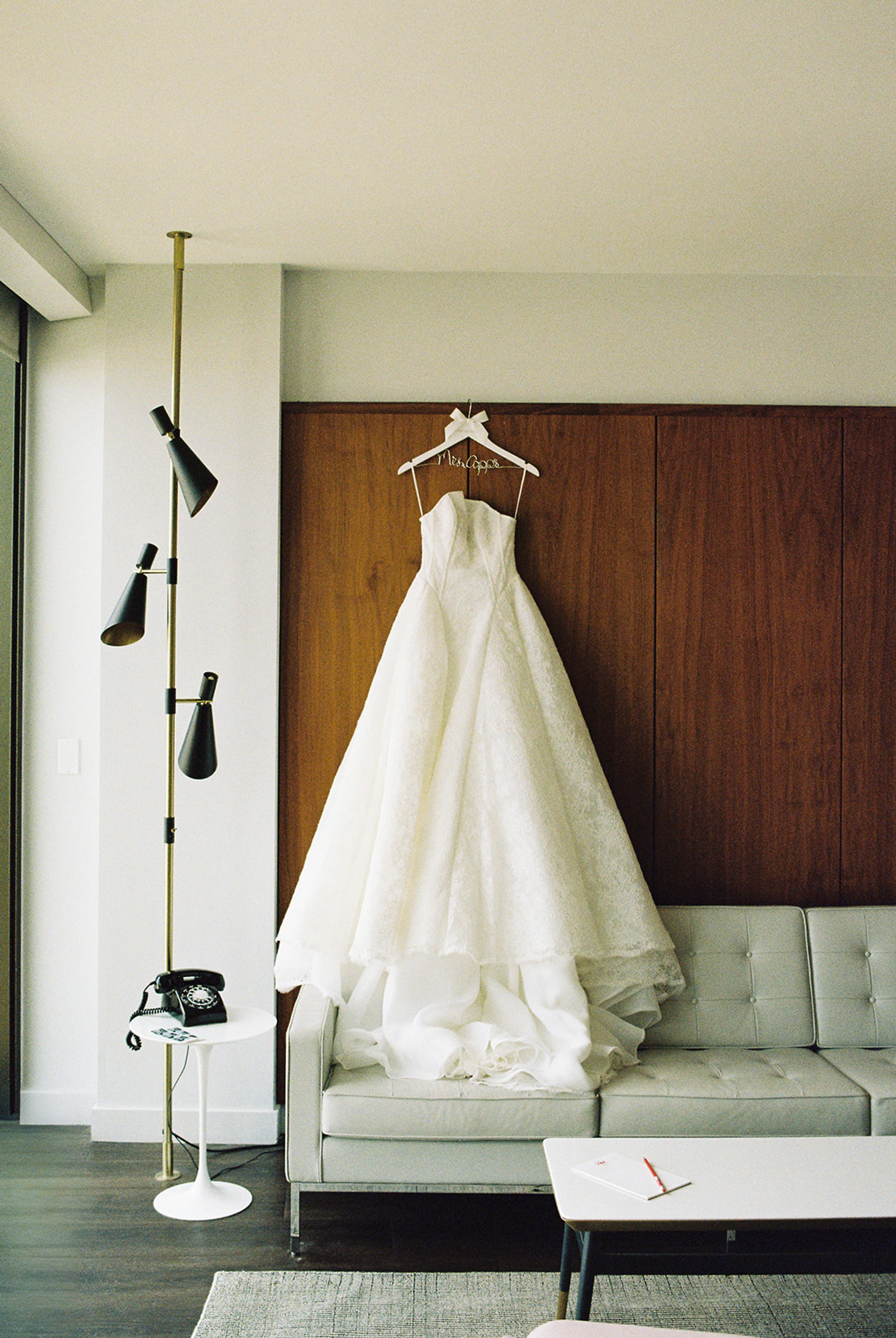 Lace ball gown wedding dress hanging on a walnut wall in a TWA Hotel guest room at JFK Airport