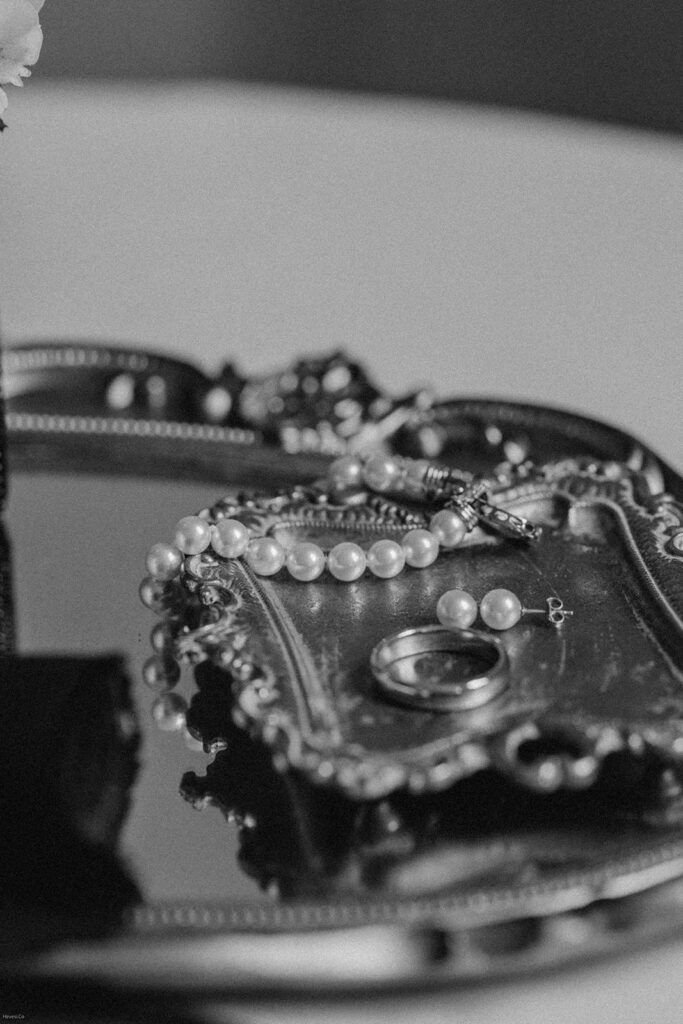 A close-up of bridal jewelry, including a pearl necklace and wedding rings, elegantly displayed on a vintage silver tray.