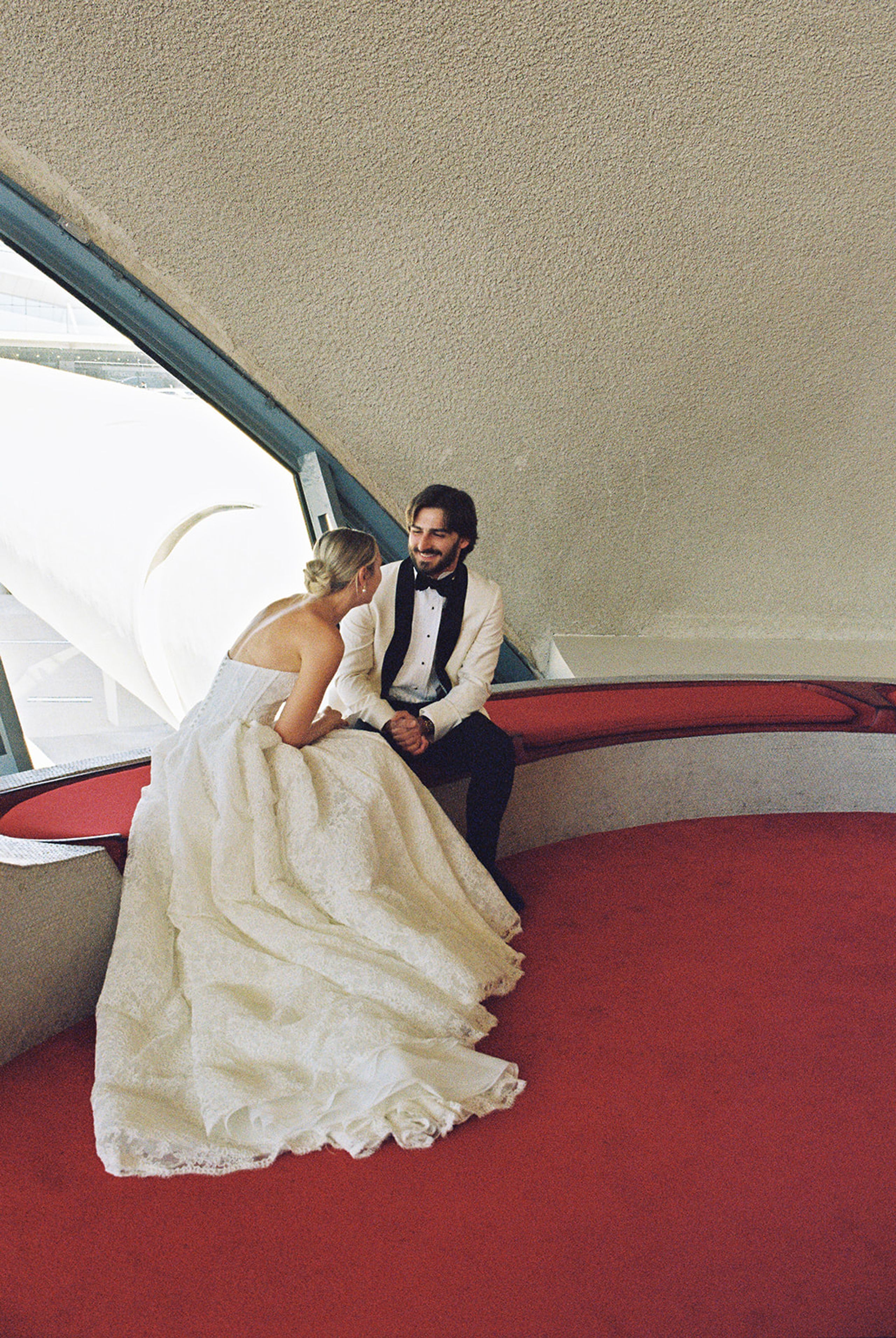 Bride and groom relaxing on red lounge seating in the TWA Flight Center terminal