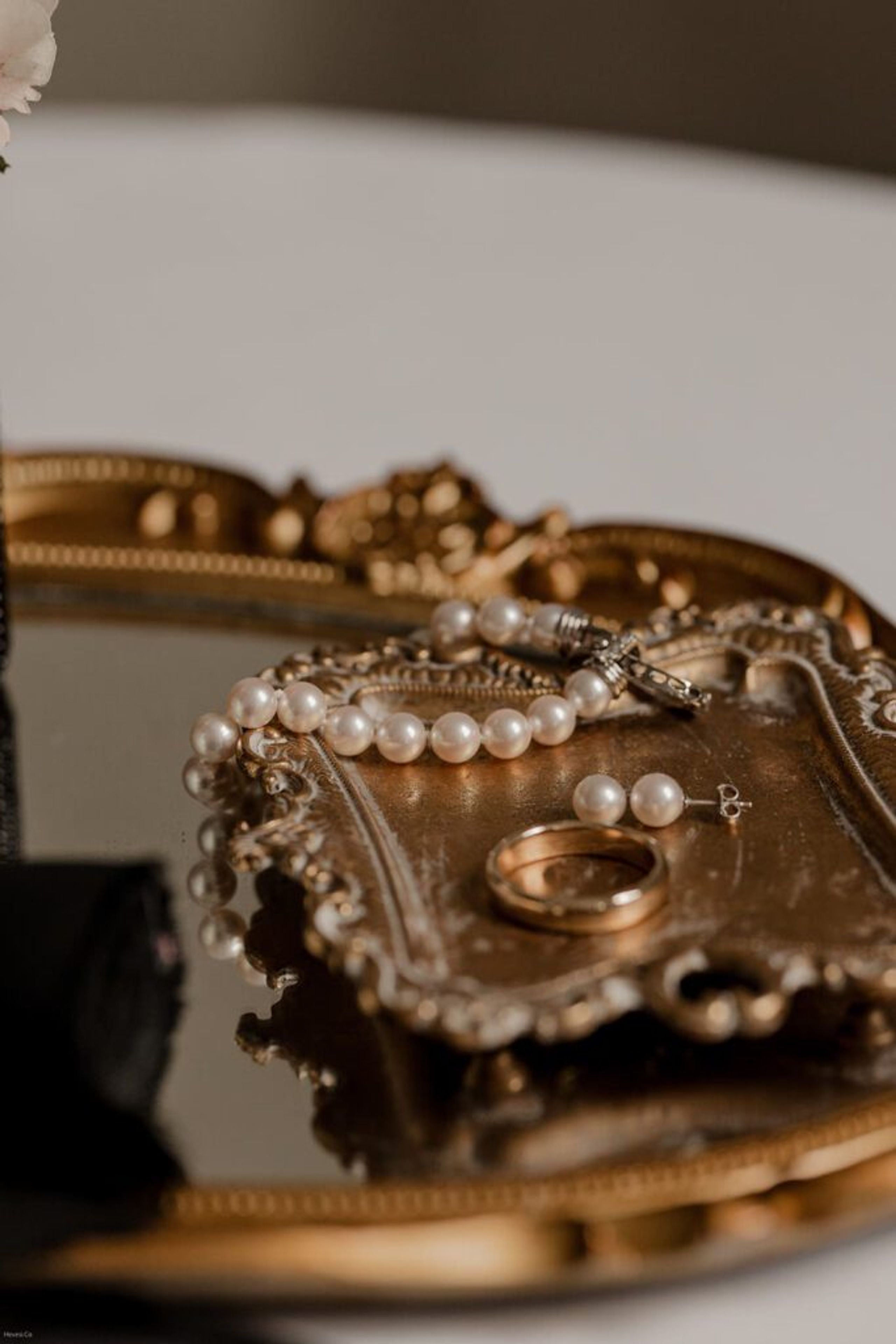 A close-up of a pearl bracelet, earrings, and a wedding ring elegantly arranged on an ornate vintage tray, reflecting the timeless details of the wedding day