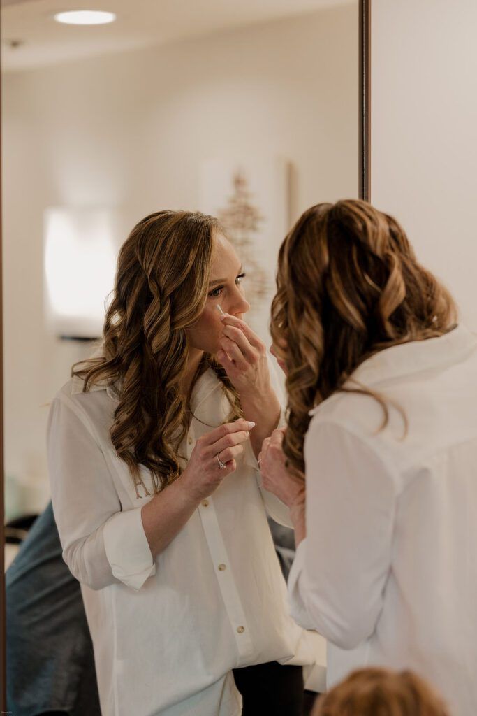Deb carefully applies makeup in front of a mirror, preparing for her wedding day at 173 Carlyle House.