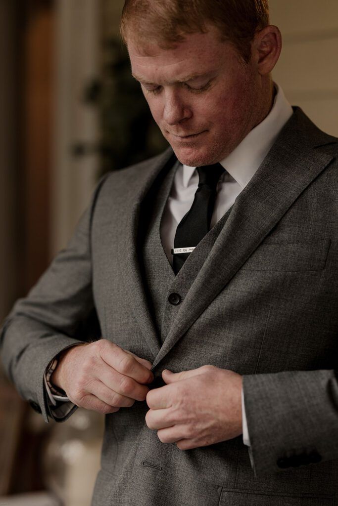 Scott carefully buttons his suit jacket, preparing for his wedding ceremony at 173 Carlyle House.