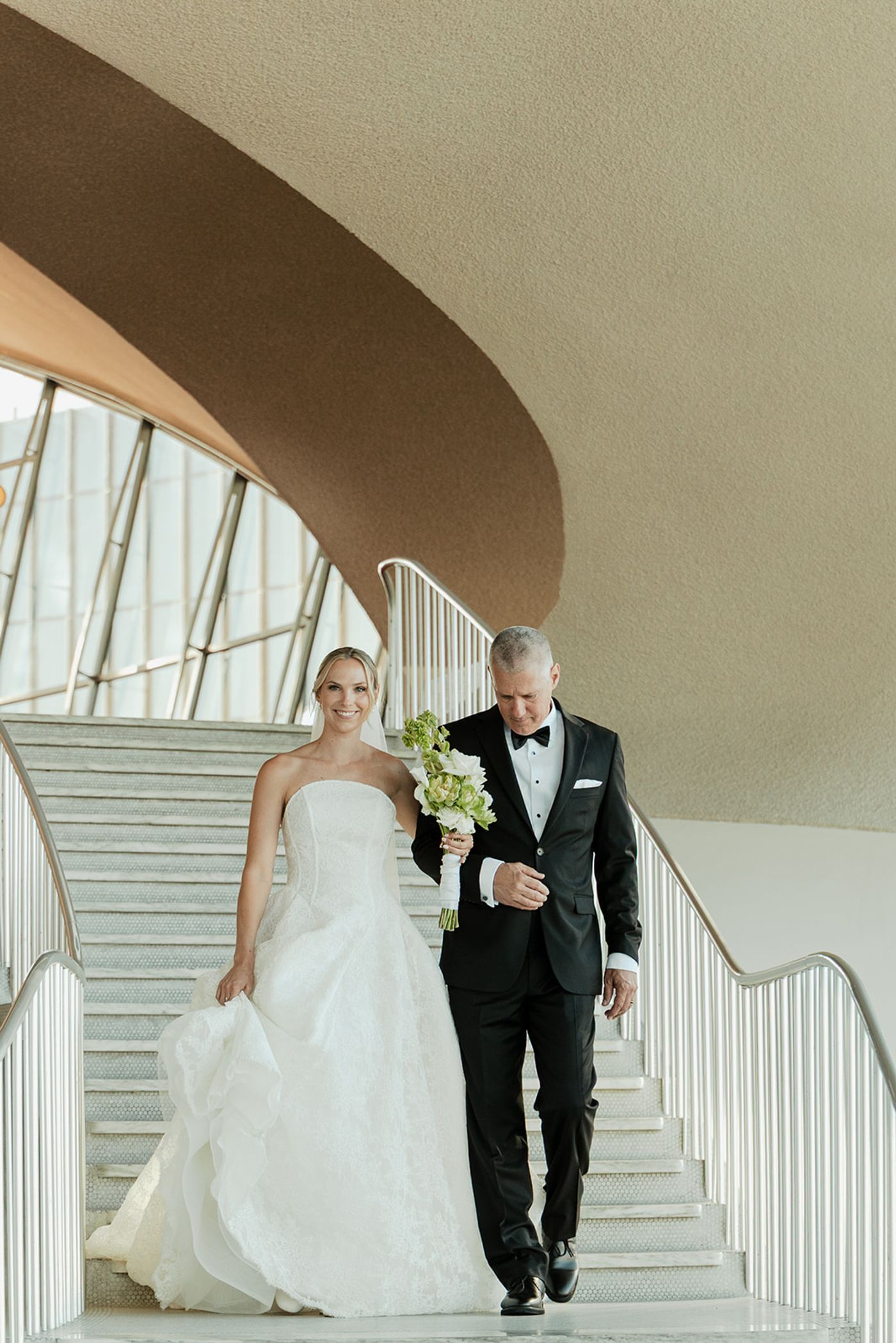 Bride walking down the TWA Flight Center staircase with her father before the ceremony