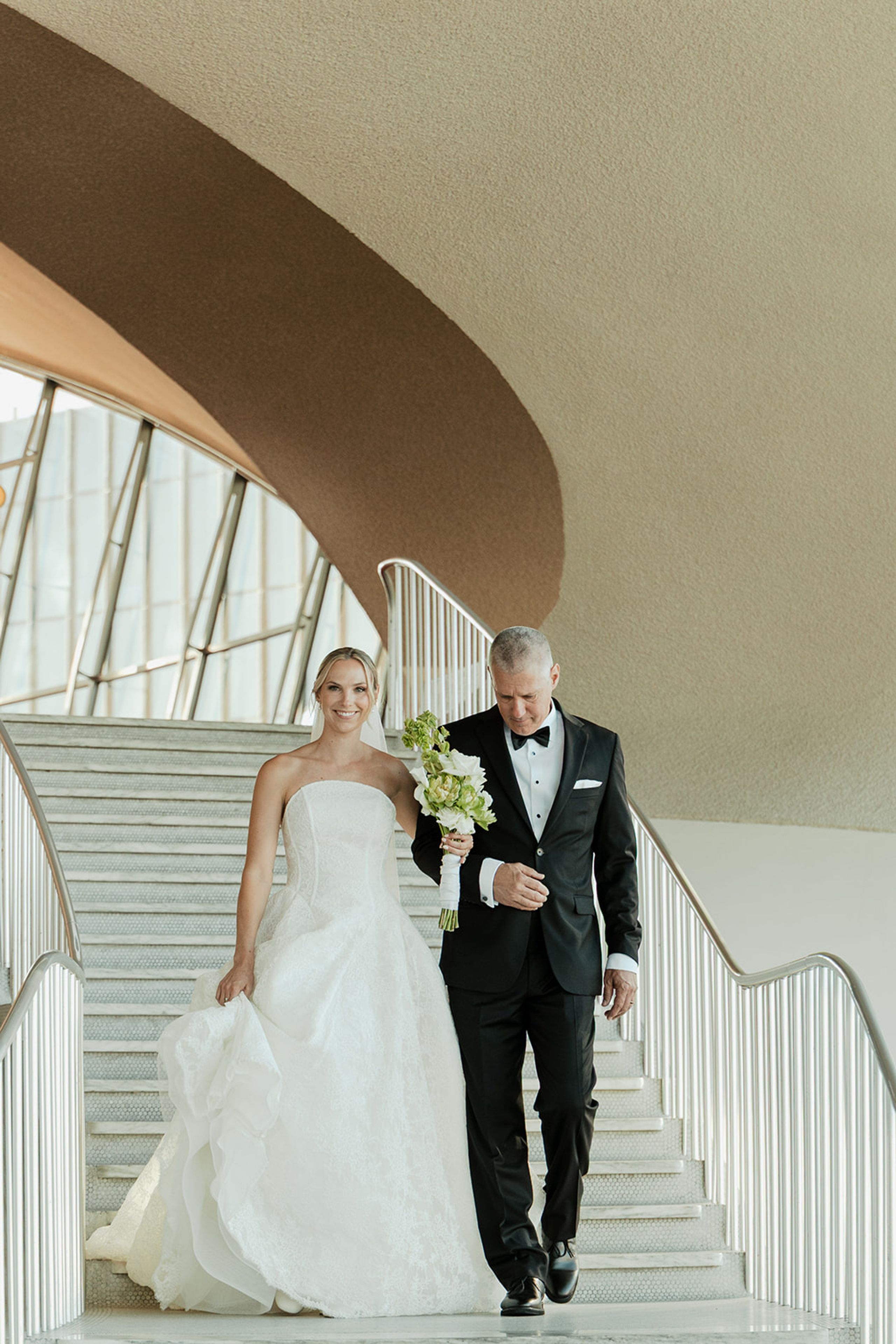 Bride walking down the TWA Flight Center staircase with her father before the ceremony
