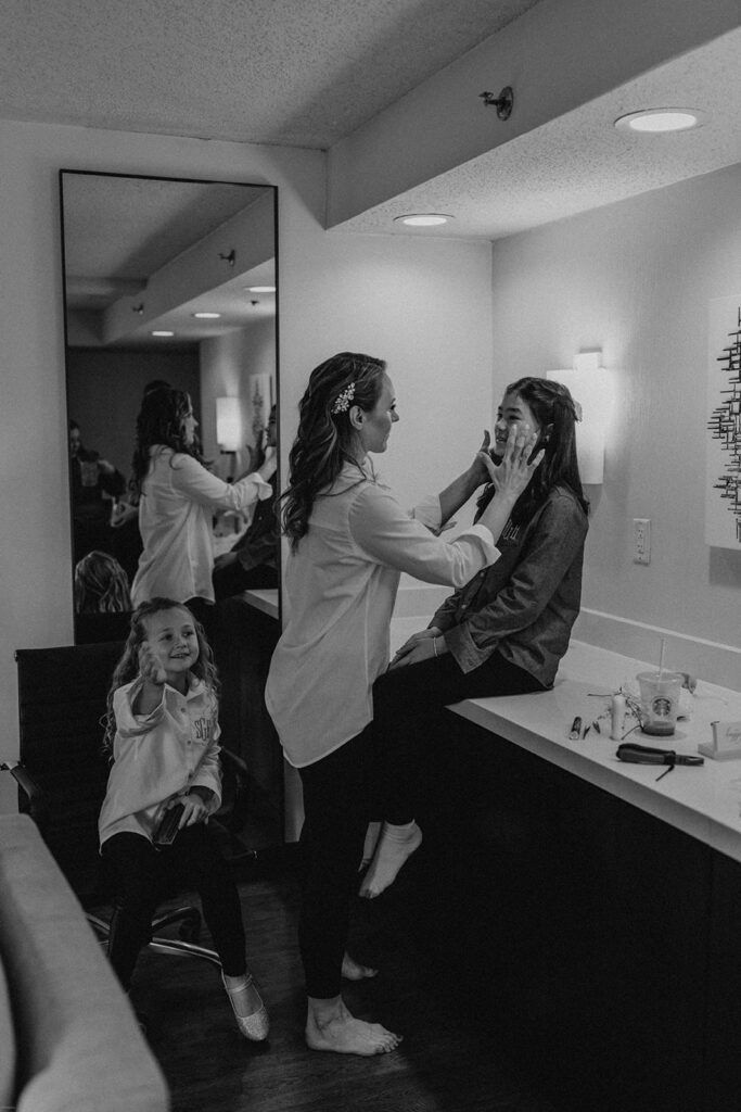 Deb carefully applies makeup to one of her bridesmaids at 173 Carlyle House, with a flower girl sitting nearby.