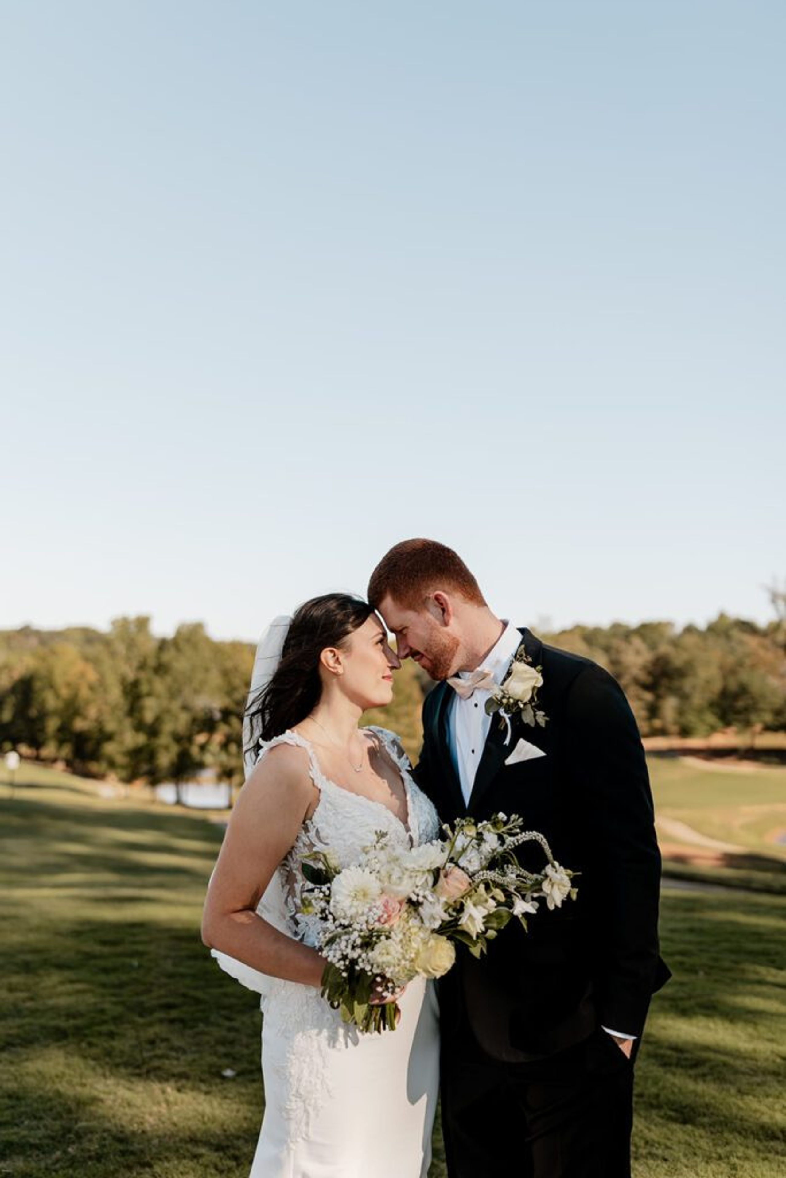 Bride and groom standing close together on the lawn at Chimney Oaks Golf Club, holding a bouquet of white flowers