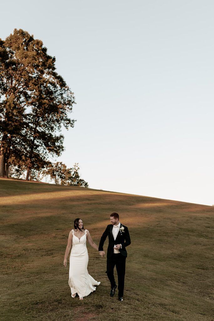Bride and groom walking hand in hand down a grassy hill during their wedding at Chimney Oaks Golf Club