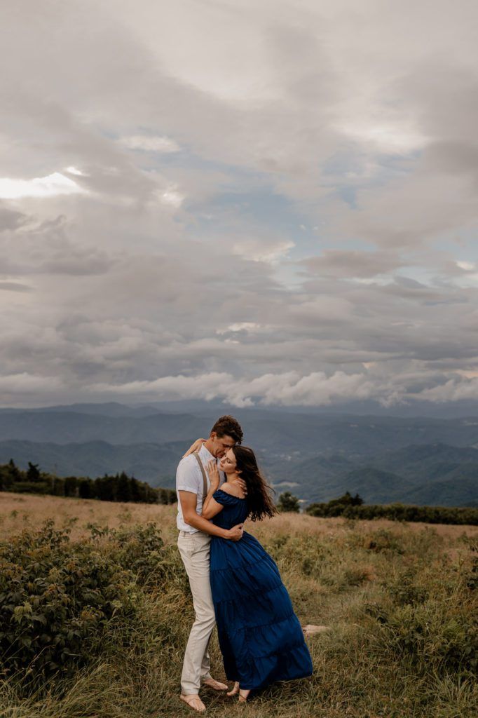 A couple embraces in a grassy field with a stunning mountainous backdrop, capturing the intimate and serene atmosphere of their Airbnb elopement.