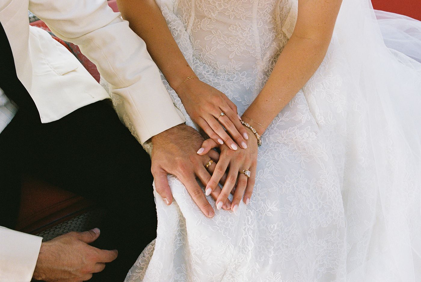 Close-up of a bride and groom's hands and wedding rings resting on her lace gown at the TWA Hotel