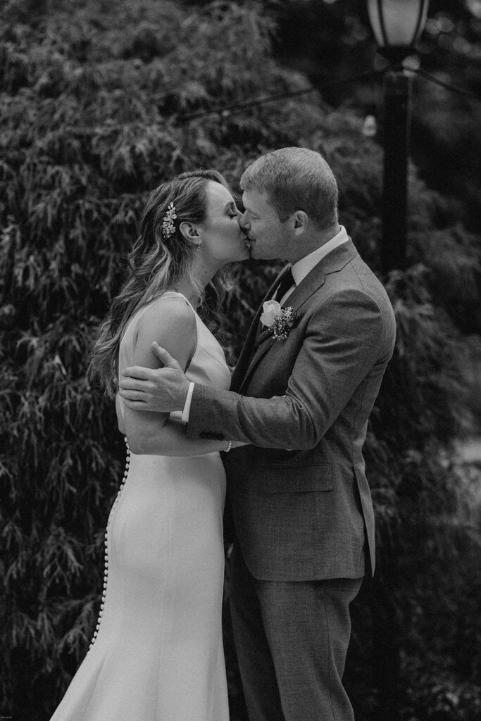 Scott and Deb share a tender kiss during their wedding ceremony, surrounded by lush greenery.