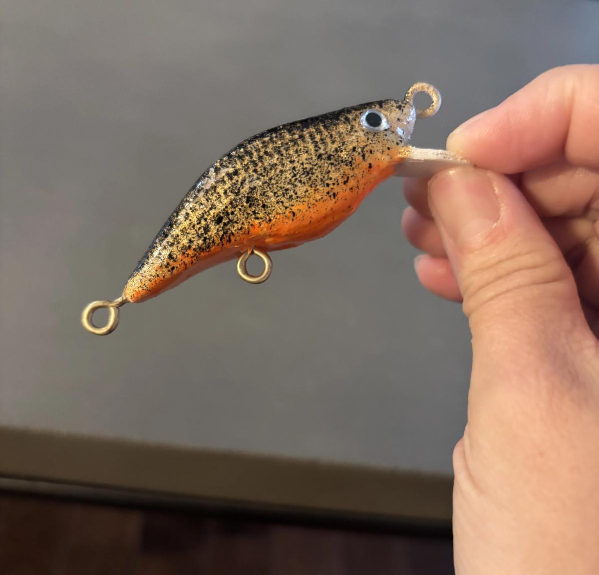 Crankbait orange et noir tenu entre deux doigts